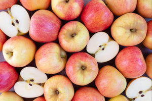A close up image of a dozen crisp apples, some whole and some cut in half, with colors varigating from pale yellow to bright red.
