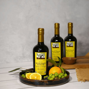 A bottle of Meyer Lemon Olive Oil with a yellow label, on a platter surrounded by fresh lemons and olives, with two more bottles in the background.