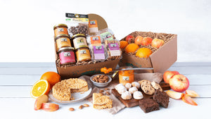 Two gift boxes laden with colorful jars of preserves, cookies, and organic fresh apples and oranges