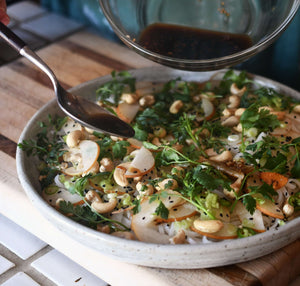 A close up image of a plated salad, featuring bits of cilantro, cashews, pear slices, and cold rice noodles.