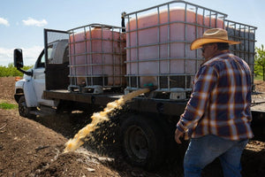 A truck carrying large containers with fruit juice, with a stream of juice pouring onto a pile of compost.
