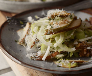 A close up image of a bright, plated salad featuring sliced pears, celery, walnuts, and cheese shavings.