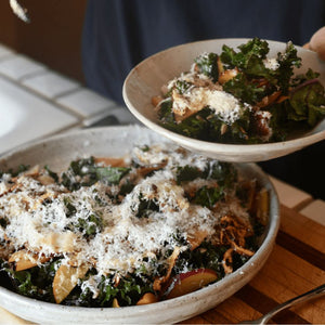 A close up image of a fresh salad consiting of dark green kale and slices of pluots, topped with shaved parmesan.