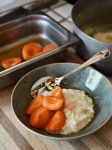 A close up image of a bowl filled with white rice pudding, topped with vibrant orange apricot slices and covered in a honey-like dressing.