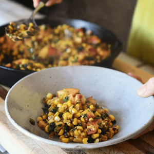 A close up image of white bowl filled with a colorful Succotash, including corn, peaches, onion, and basil.