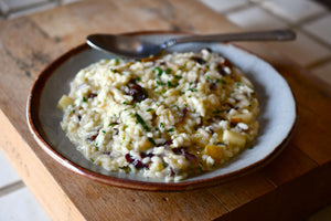 A close up image a bowl of Risotto that is a creamy consistency with bits of dried cherries and green garnish.