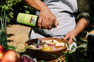 A close up image of someone pouring a bottle of olive oil over a fresh salad.