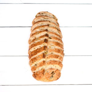A close up flatlay of a rustic, golden loaf of bread with bits of olives in it, cut into thin, artfully displayed slices.