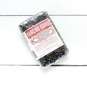 Medium sized black glossy beans in a sealed bag on a white flat lay.