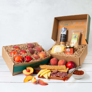 Two rustic gift baskets filled with juicy peaches and nectarines, and packaged salami, cheese, crackers, and jelly.