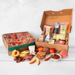 Two rustic craft gift baskets featuring juicy peaches and nectarines, and artfully packaged charcuterie goods.