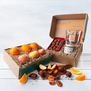 Two rustic craft gift baskets featuring vibrant citrus oranges and crisp apples, and artfully packaged honey, truffles, and dried fruit.