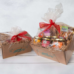 Two rustice gift baskets wrapped in cellophane, the first filled with peaches and nectarines, and the second filled with a variety of packaged goods.