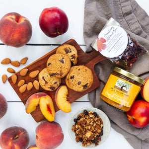 An artful spread of cookies, almonds, and granola on a wooden serving board, sourrounded by fresh, juicy peaches and nectarines, and Frog Hollow peach conserve.