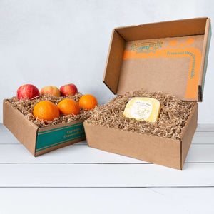 Two rustic craft gift baskets featuring vibrant citrus oranges and crisp apples, and artfully packaged Bellwether Farms Carmody Cheese.