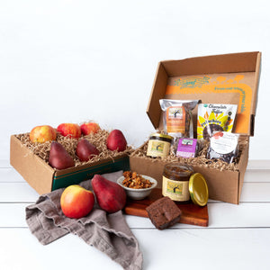 Two rustic craft gift baskets featuring juicy pears and crisp apples, and artfully packaged granola, marmalade, brownie, tea, and chocolate covered pistachios.