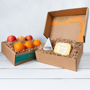 Two rustic craft gift baskets featuring vibrant citrus oranges and crisp apples, and artfully packaged Point Reyes blue cheese and Bellwether Farms Carmody Cheese.