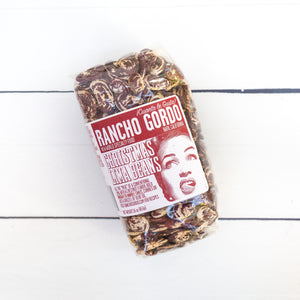 large beans, cream colored with red splashes across each one packaged in a sealed bag on a white flat lay.
