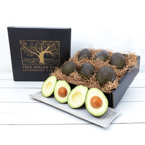 An elegant gift box with a gold embossed tree filled with dark green avocados.
