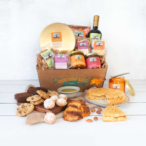 A craft gift basket filled with artfully packaged products, including baked goods, fruit conserves, almonds, dried fruit and olive oil.