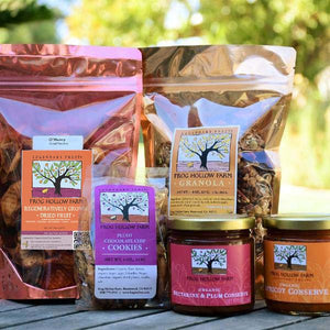 A close up image of nicely packaged granola, dried fruit, cookies, and colorful fruit conserves on a wooden table.