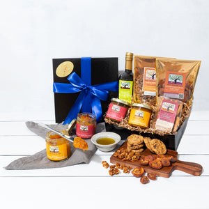 A gift box wrapped in a vibrant bow, filled with artfully packed cookies, fruit conserves, granola, dried fruit and olive oil.
