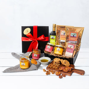 A gift box wrapped in a vibrant bow, filled with artfully packed cookies, fruit conserves, granola, dried fruit and olive oil.