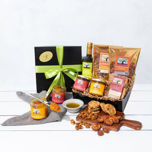 A gift box wrapped in a vibrant bow, filled with artfully packed cookies, fruit conserves, granola, dried fruit and olive oil.
