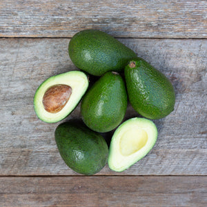 A close up image of vibrant, dark green avocados with buttery flesh, set against a rustic wooden background.