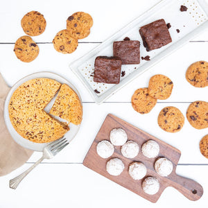 A flat lay image featuring a variety of delicious baked goods, artfully displayed on platters and a white background.
