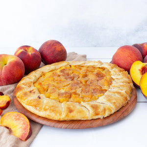 An exquisite peach galette, filled with juicy yellow peaches, cradled in a golden pastry crust, on a wooden serving board, surrounded by fresh peaches.
