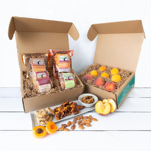 Two rustic craft gift baskets with an assortment of vibrant fruit, and artfully packaged granola, cookies, dried fruit, and fresh nuts.