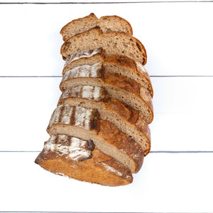 A flatlay image of a loaf of rustic, artisan bread with crunchy golden crust, cut into even slices, showcasing the fluffy interior of the loaf.