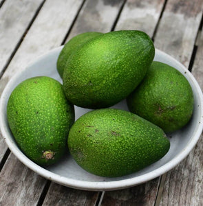 A close up image of, vibrant green avocados in a bowl, sitting on a rustic wooden table.
