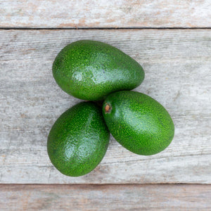 A close up image of three vibrant green avocados against a rustic wooden background.