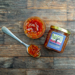 A flat lay of a jar containing bergamot orange marmalade with a colorful Frog Hollow label, next to spoonful of marmalade.