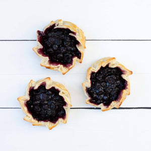 A flat lay featuring three handmade tartlets, filled with delicious juicy blueberries, cradled within golden pastry.