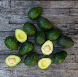 A square image of several dark green, buttery avocados laying against a rustic wooden background.