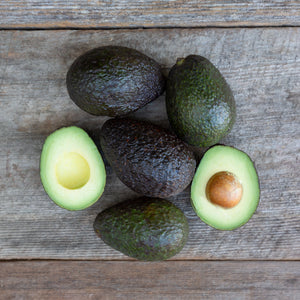 A close up image of vibrant, dark green avocados with buttery flesh, set against a rustic wooden background.