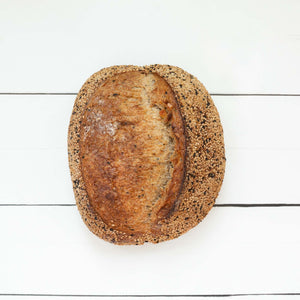 A flatlay image of a loaf of rustic, artisan bread with crunchy golden crust, set against a white wooden crust.