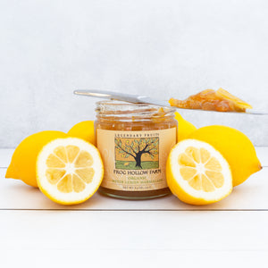 A jar filled with yellow meyer lemon marmalade, surrounded by exquisite, juicy lemons, on a white table.