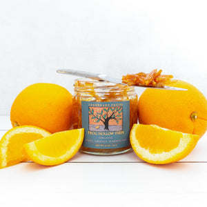 A jar filled with navel orange marmalade, surrounded by exquisite, juicy orangess, on a white table.