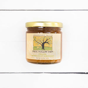 A flat lay image of a jar containing organic meyer lemon marmalade with a Frog Hollow Farm label, against a rustic white table. 