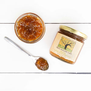 A flat lay of a jar containing a organic meyer lemon marmalade with a Frog Hollow label, next to spoonful of marmalade.