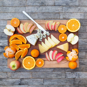 An artully designed charcuterie spread, featuring a varies of fresh, juicy fruit slices, such as vibrant oranges and crisp apples, centered around sliced blocks of carmody cheese and blue cheese.