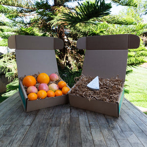 Two rustic craft gift baskets sitting atop a wooden table, one filled with a variety of colorful, fresh fruit and the other filled with packaged Point Reyes Original Blue Cheese.