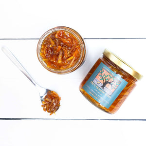 A flat lay of a jar containing a organic navel orange marmalade with an artfully designed Frog Hollow label, next to spoonful of marmalade.
