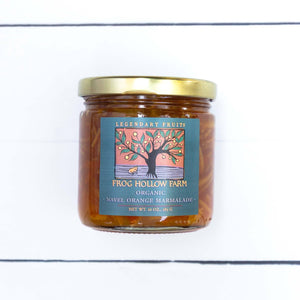 A flat lay image of a jar containing Navel Orange marmalde with an artful Frog Hollow Farm label, against a rustic white table. 