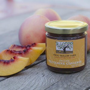 A jar full of Frog Hollow's organic nectarine conserve, surrounded by fresh, juicy nectarines on a rustic wooden table.