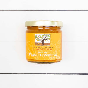 A flat lay image of a jar containing a bright yellow peach conserve with a Frog Hollow Farm label, against a rustic white table background. 